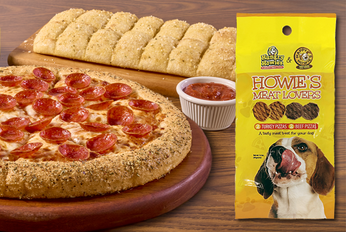 There is an array of a pepperoni pizza on a wooden plate, a white cup of marinara sauce , sliced Howie Bread, and a yellow bag of Happy Howie's dog treats with a dog licking its mouth on the front. 