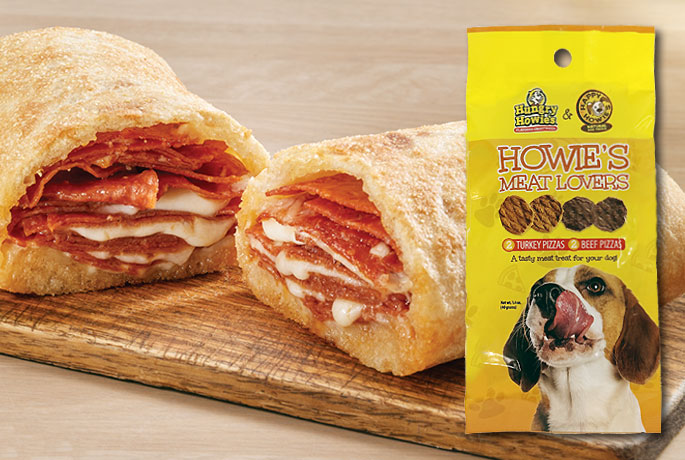 Melted cheese and pepperoni in a roll sitting on a wooden plate. A yellow bag of dog treats with a dog licking it's mouth on the cover.