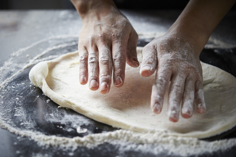 Hands spreading pizza dough in flour. 