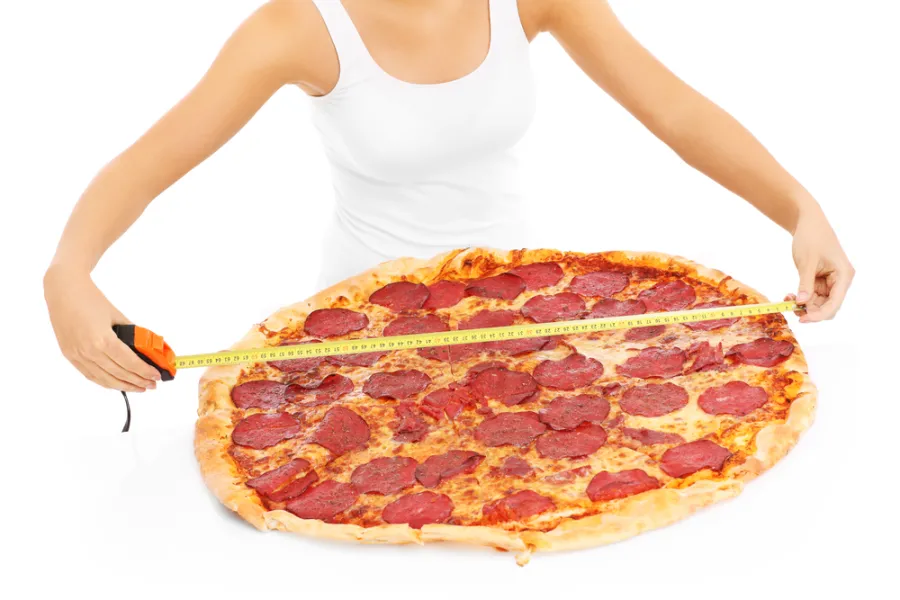 Woman measuring a large pizza with a measuring tape