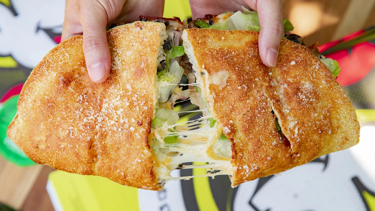 Hungry Howie's Oven Baked Sub being pulled apart with delicious cheese, lettuce, olives, and mushrooms inside 